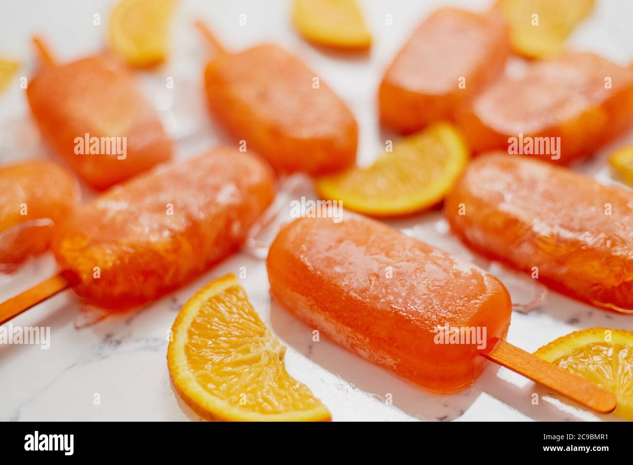 Pop sicle surgelate fatte in casa con arance fresche oragniche poste con cubetti di ghiaccio sul tavolo di marmo Foto Stock