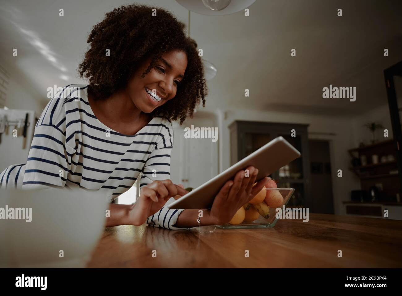 Donna felice appoggiata al bancone della cucina guardando i video di cucina in un tablet digitale in cucina Foto Stock