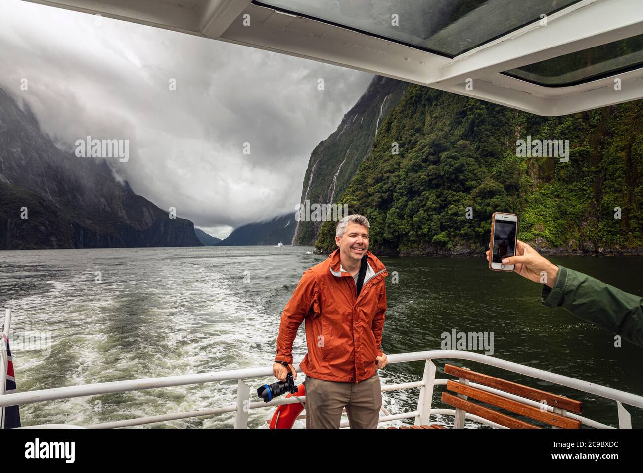 Tourist avendo la sua foto scattata durante una gita in barca a Milford Sound in un giorno tempestoso, Fiordland National Park, Southland, South Island, Nuova Zelanda Foto Stock