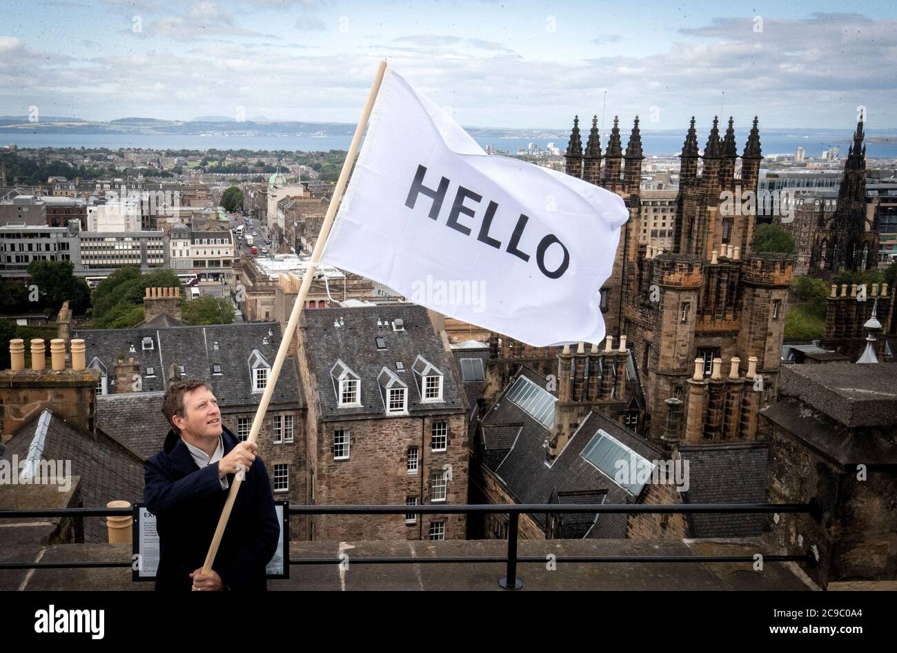 L'artista Peter Livissige vola una delle sue bandiere HELLO sopra i tetti di Edimburgo mentre rivisita la sua commissione 2013 Festival d'Arte di Edimburgo Bandiere per Edimburgo, che invitava gli edifici in tutta la città a battere una bandiera bianca che recita CIAO. Foto Stock
