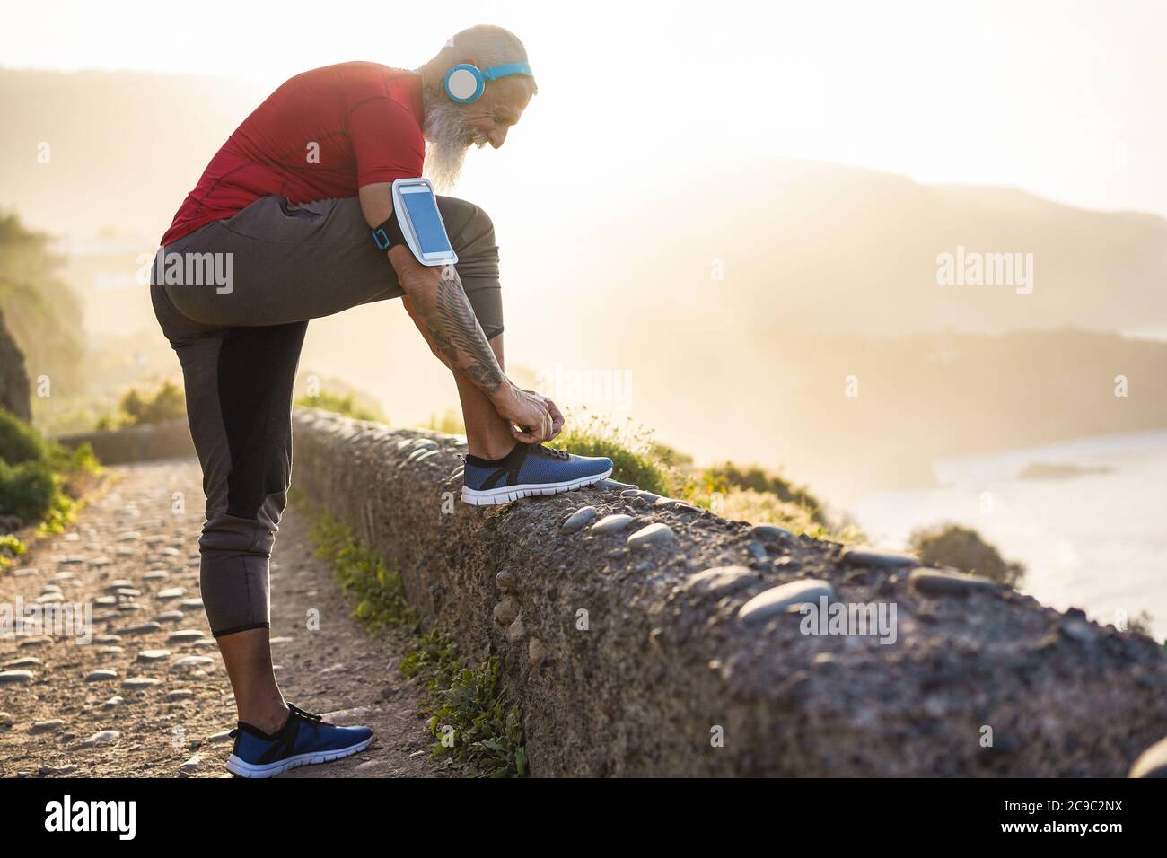 Uomo tatuaggio fit le sue scarpe sportive all'aperto durante la sessione di jogging - allenamento e fitness stile di vita concetto - Focus sulle mani Foto Stock