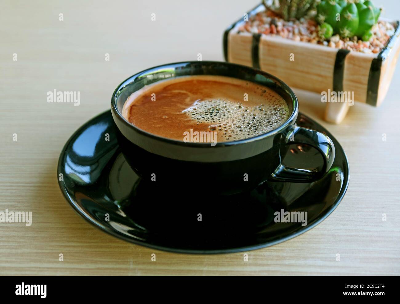 Closeup una tazza di caffè caldo schiumoso con pianta in vaso blurry su tavolo di legno Foto Stock