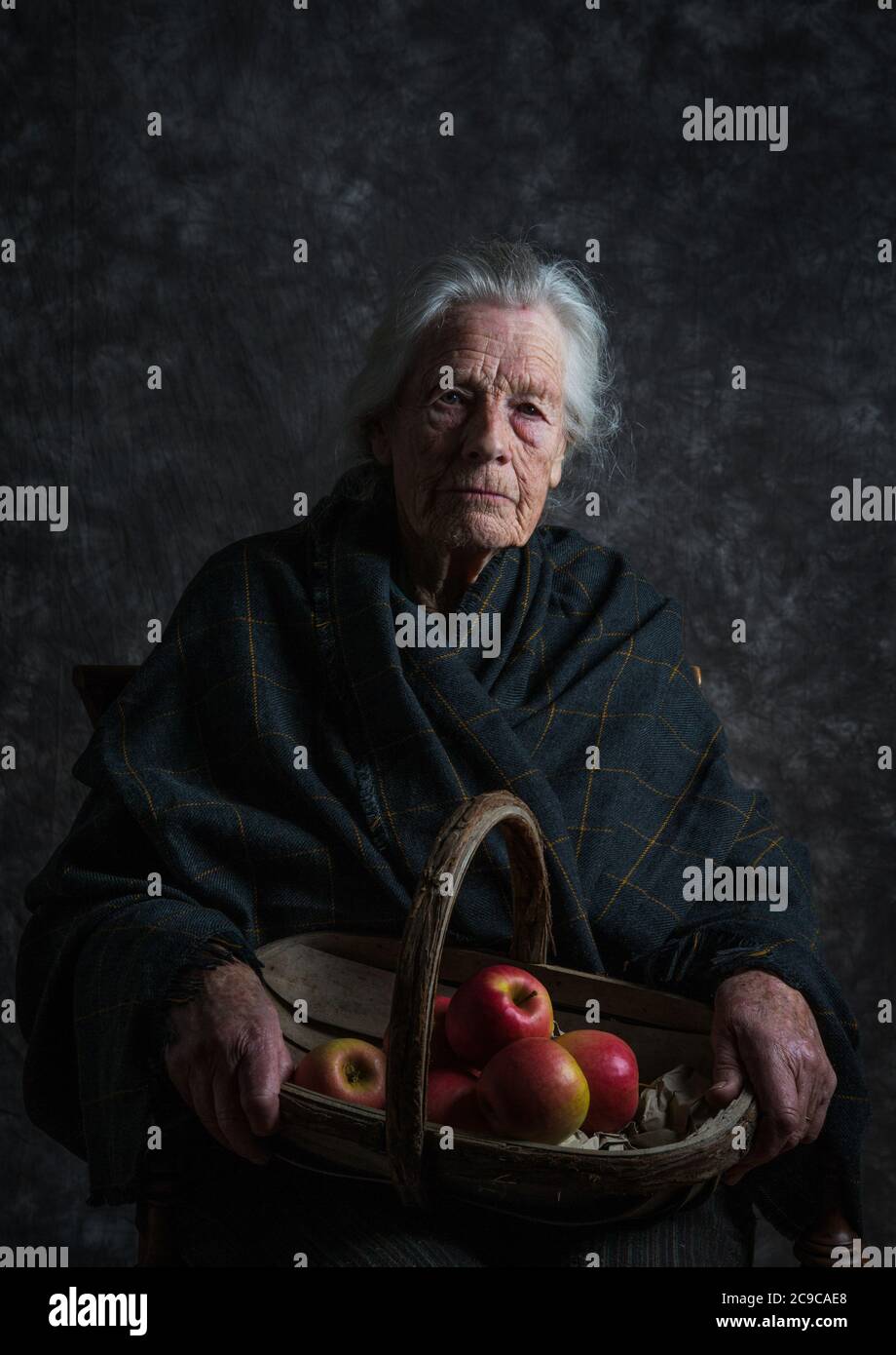 Donna con capelli grigi indossando scialle che tengono un cesto di mele Foto Stock