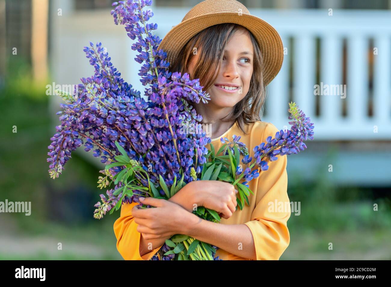 Una ragazza sorridente tiene in mano un bel bouquet grande di lupino. Un bambino in un cappello di paglia. Giorno estivo soleggiato. Foto Stock
