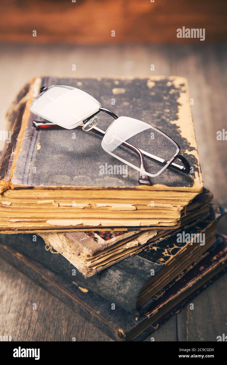 gli occhiali giacciono sul mucchio di libri vecchi e obsoleti in uno studio Foto Stock