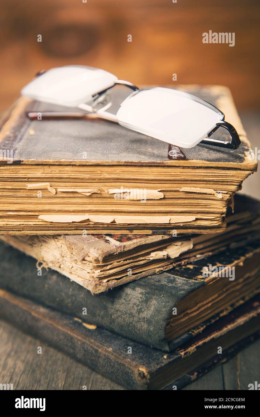 gli occhiali giacciono sul mucchio di libri vecchi e obsoleti in uno studio Foto Stock