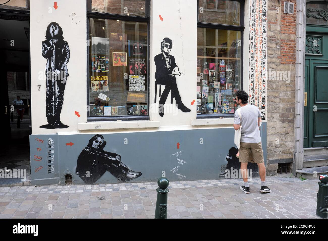 Bruxelles, Belgio un passer di soste per navigare in un negozio di dischi vetrina che è anche coperto di stencil art di famose star pop rock luglio 2020. Foto Stock