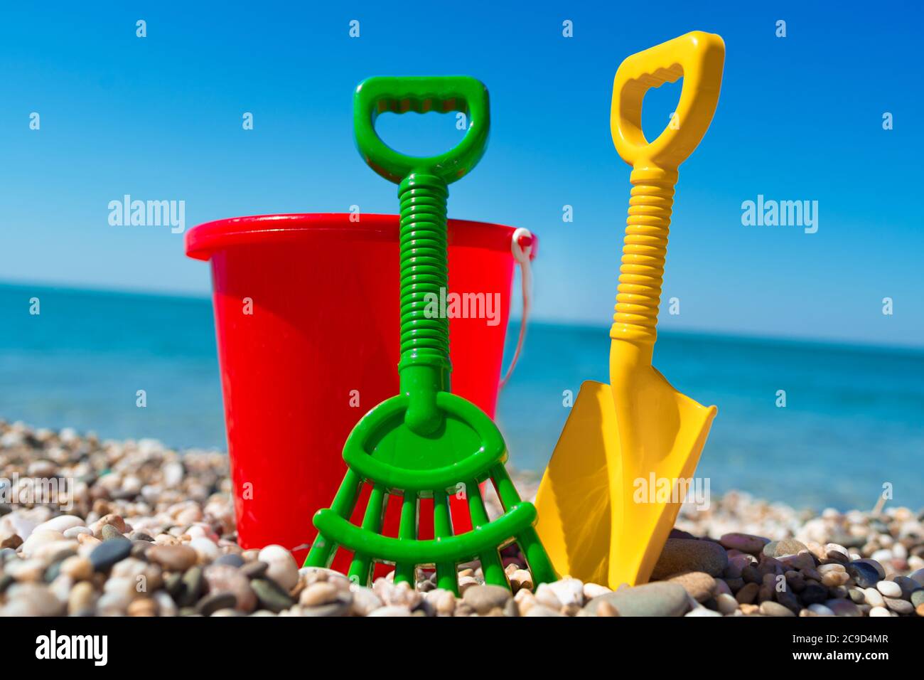 Secchio giocattolo e vanga sulle pietre della spiaggia Foto Stock