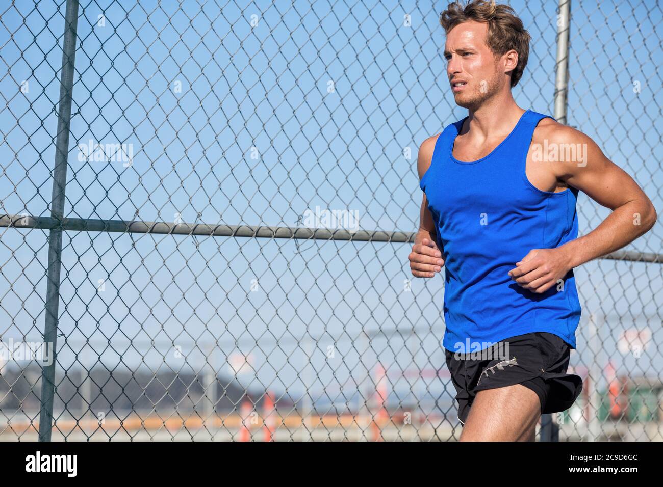 Atleta sano runner man - vita urbana. Giovane sport maschile running in grunge recinzione sfondo all'aperto in estate indossando il top serbatoio blu Foto Stock