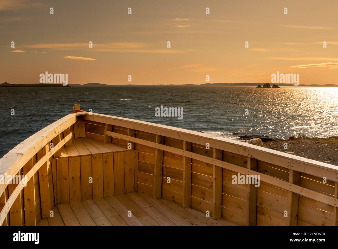 Arco di legno di una barca da pesca con l'oceano sullo sfondo. L'orizzonte del mare è arancione luminoso con un po' di cielo blu, sporadiche nuvole e piccole isole. Foto Stock