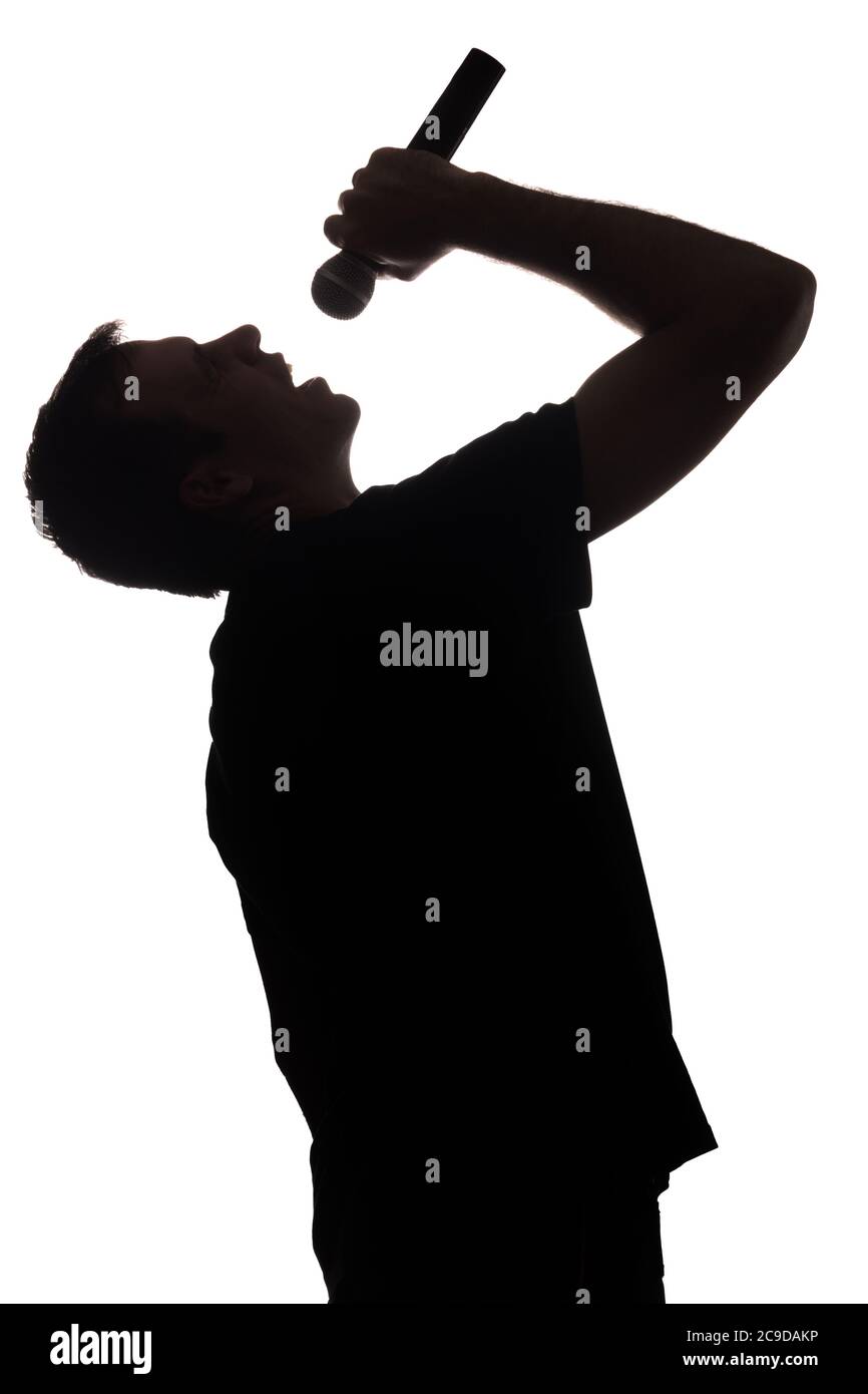 Giovane uomo che canta nel microfono, alzando le mani - silhouette Foto Stock