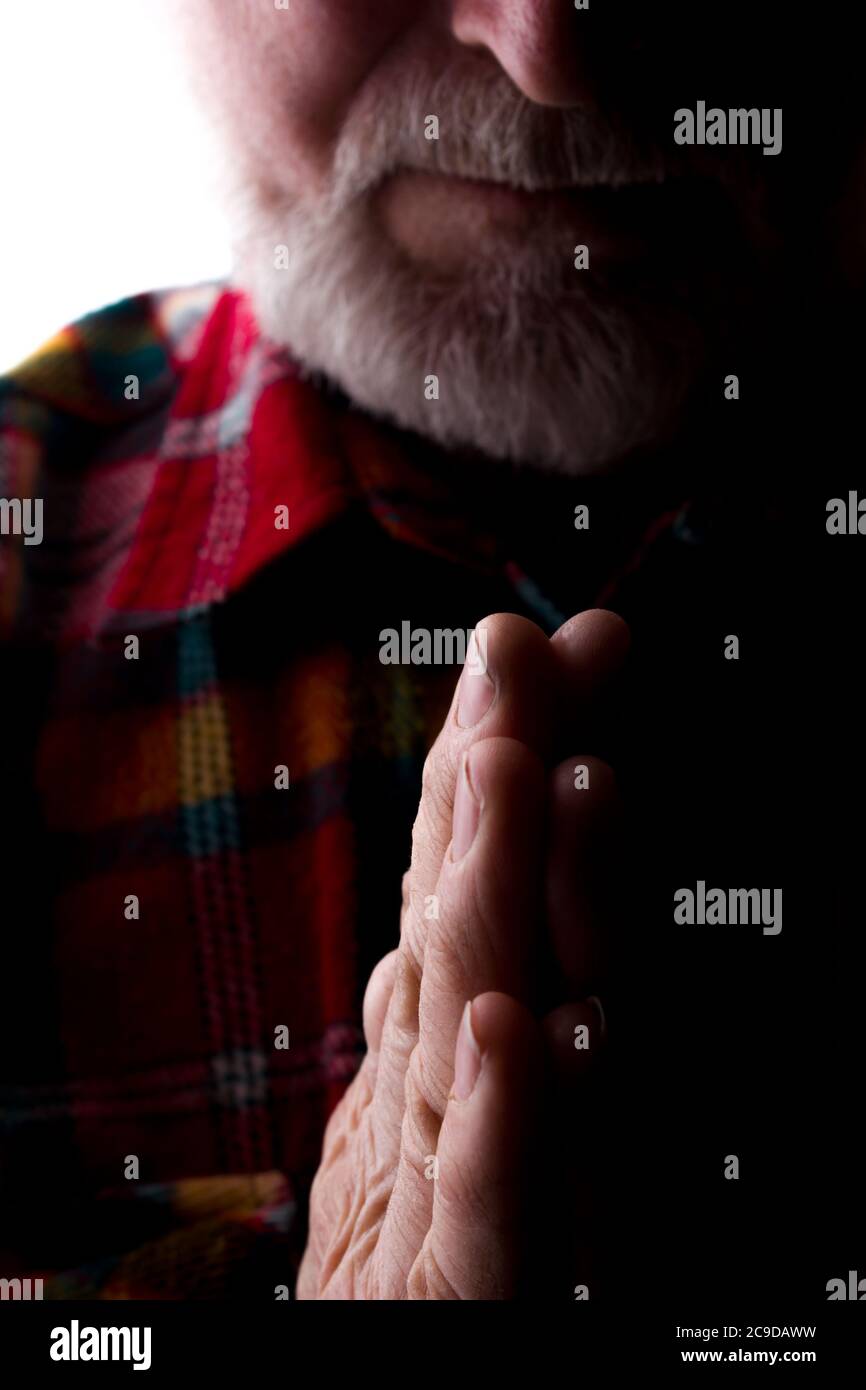 Un uomo con una barba all'età tiene insieme le mani, una preghiera e una richiesta - silhouette, isolare Foto Stock