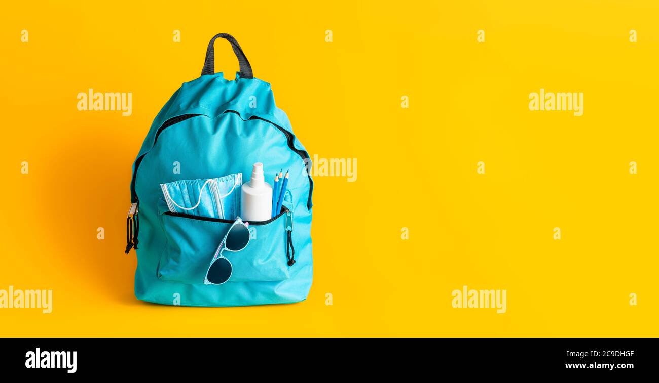 Concetto di ritorno a scuola durante la pandemia di Corona. Borsa con maschere mediche, disinfettanti e matite isolate su sfondo giallo. Nuove regole scolastiche Foto Stock
