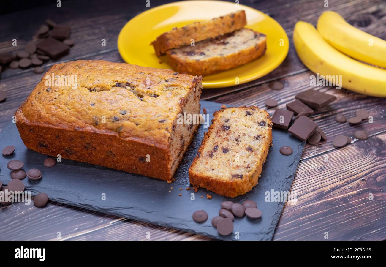Pane alla banana sul tagliere con gocce di cioccolato e banana fresca sullo sfondo. Foto Stock