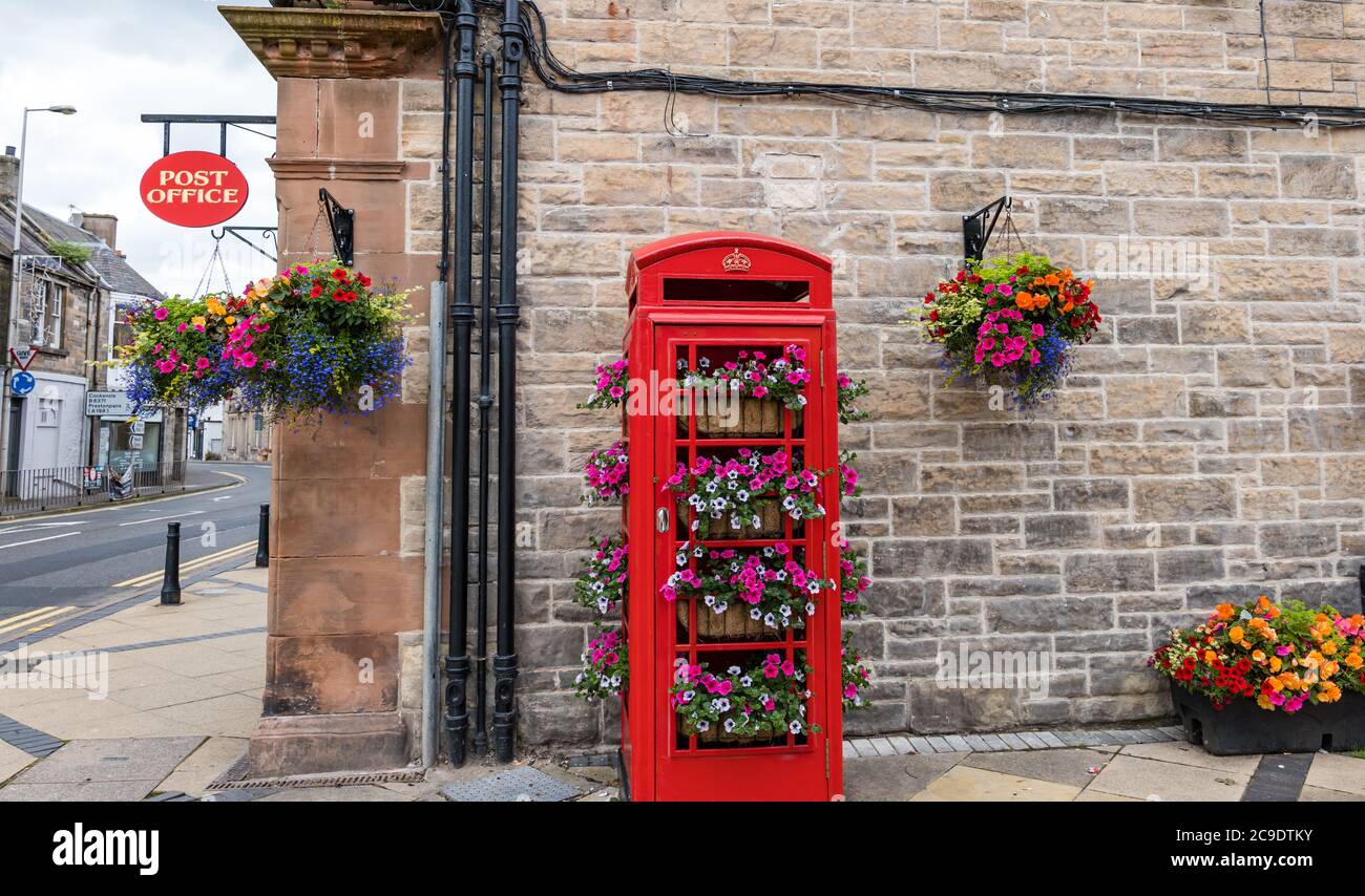 Iconico telefono rosso britannico convertito in cestini di fiori e segno dell'Ufficio postale, Tranent, East Lothian, Scozia, Regno Unito Foto Stock