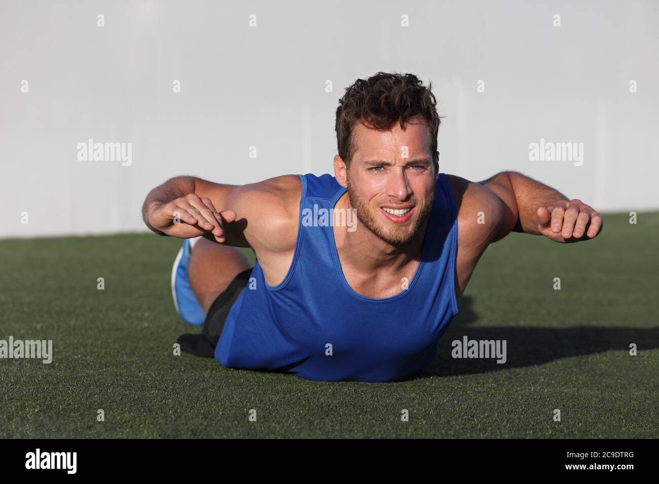 Fitness allenamento indietro grasso esercizio fisico uomo che fa superman variazione di allenamento corpo inferiore. Atleta forte che si allenano all'aperto in erba del parco. Abbassare Foto Stock