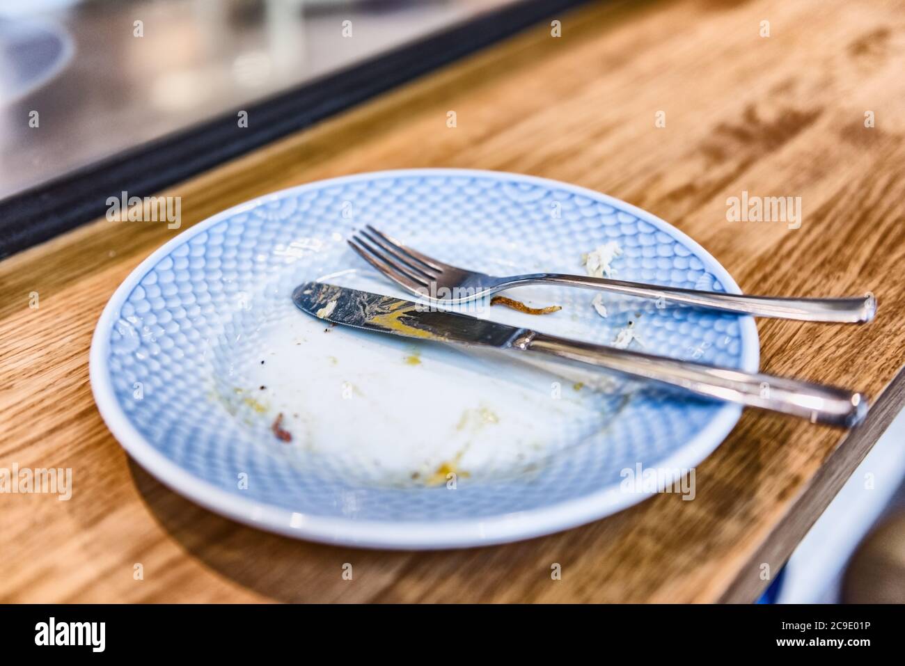 Piatto vuoto dopo il pasto finito al ristorante - forchetta e coltello riposati sulla cena fatta con briciole al banco bistrot. Foto Stock