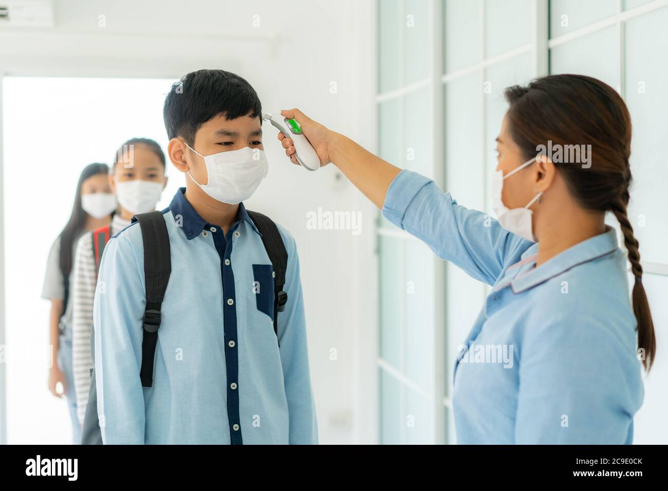 Insegnante di donna asiatica che usa termometro temperatura di screening studente per la febbre contro la diffusione di COVID-19, mentre studente tornare a scuola, nuovo Foto Stock