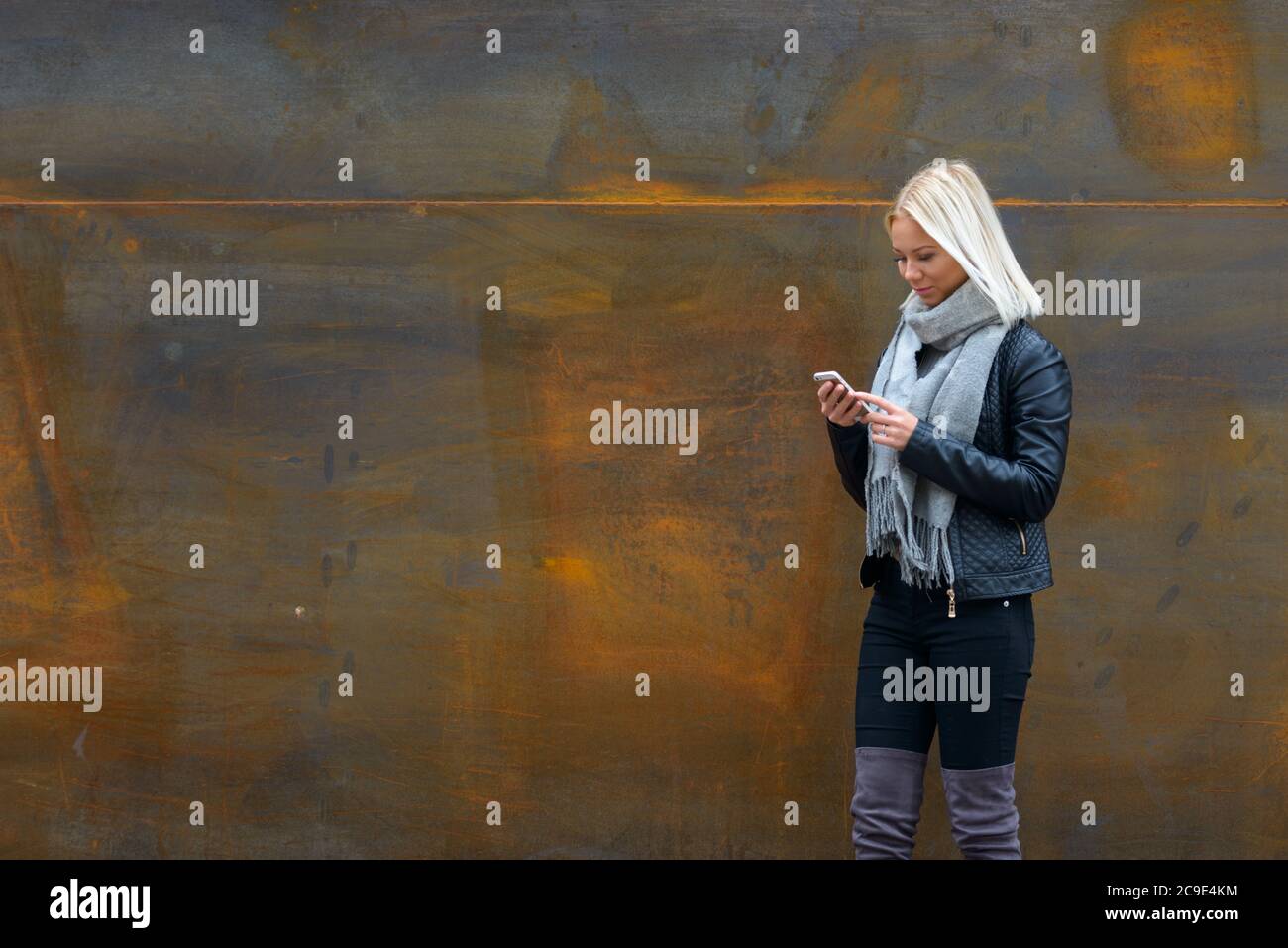 Giovane bella donna bionda che usa il telefono cellulare contro il vecchio muro di metallo arrugginito Foto Stock