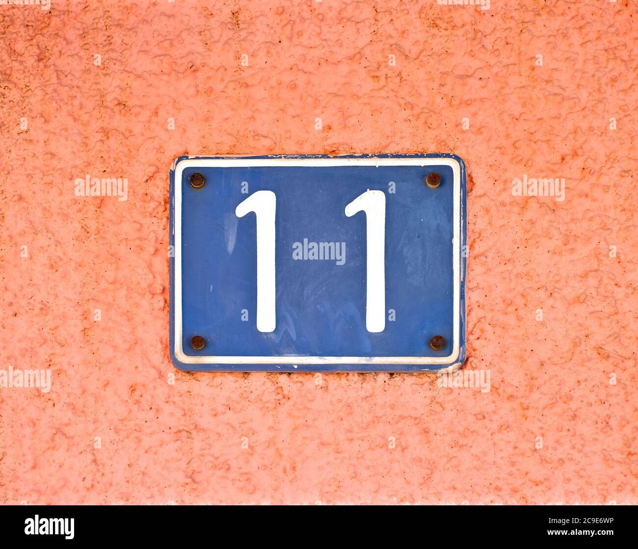 Numero 11 / undici, piastra blu sulla superficie della parete rosa pallido. Foto Stock