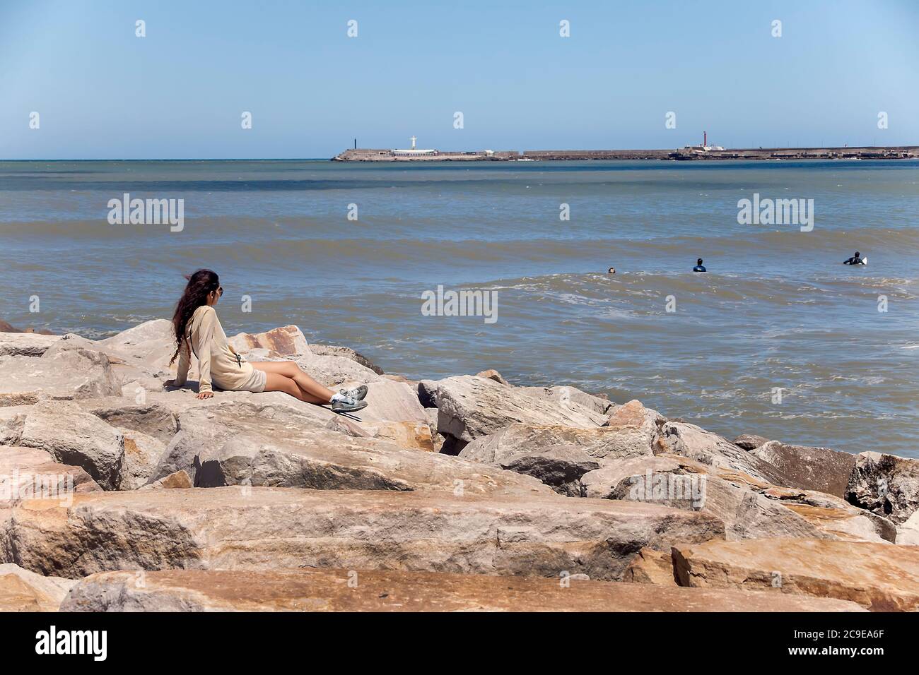 Donna in breakwater guardando surfisti in mare al largo di Mar del Plata, Provincia di Buenos Aires, Argentina Foto Stock