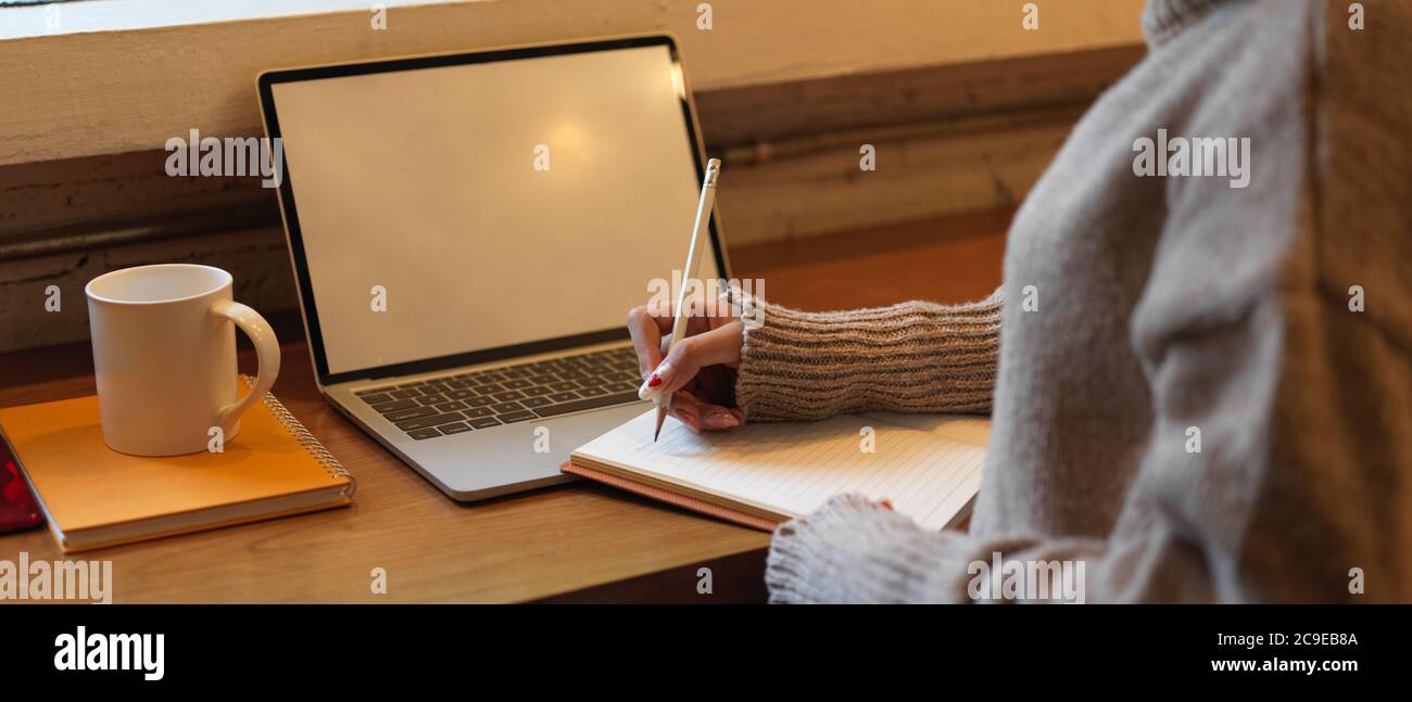 Un'immagine ritagliata di una studentessa universitaria che fa i compiti con un computer portatile in mock-up sul bancone bar della caffetteria Foto Stock