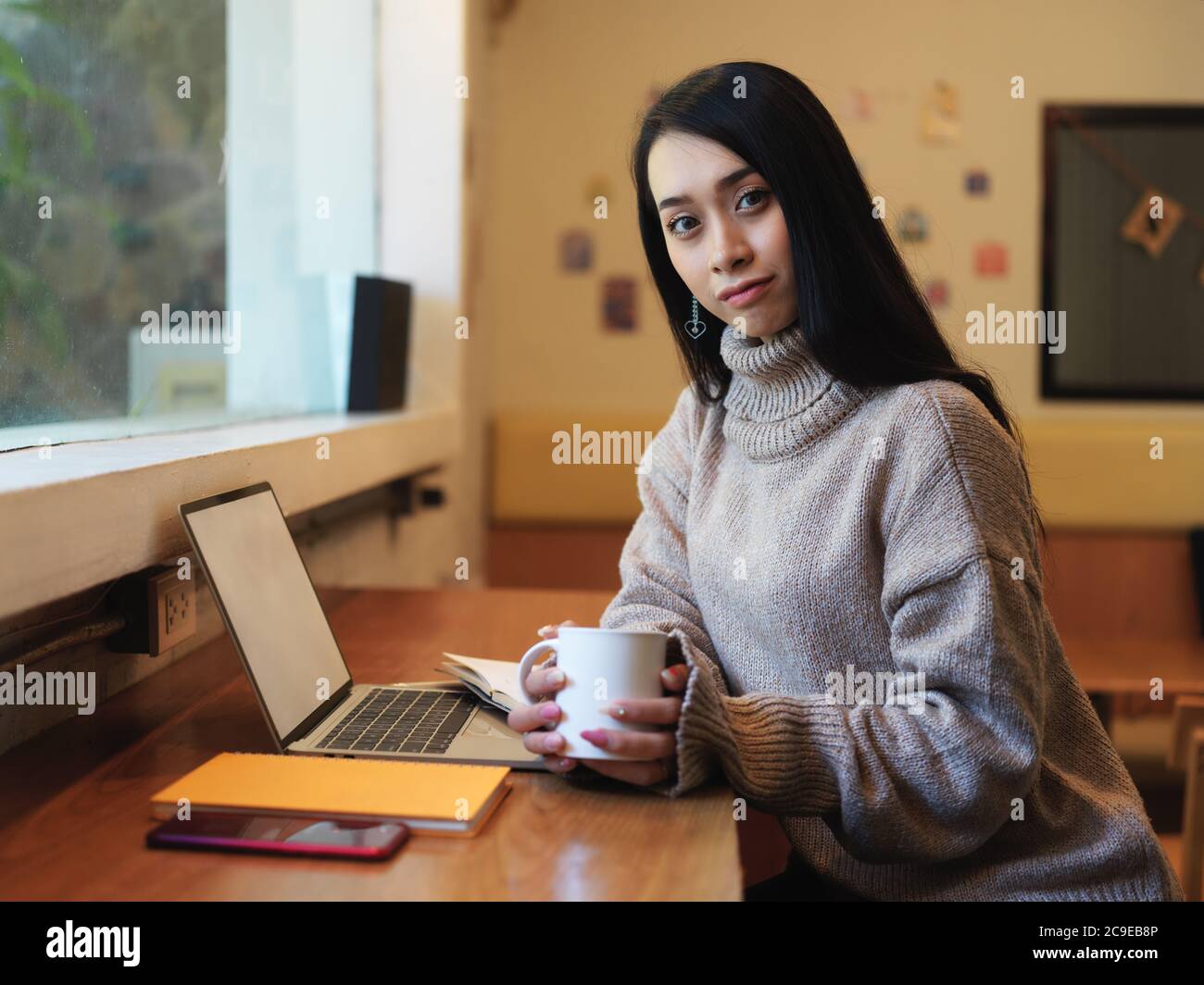 Ritratto di una studentessa universitaria seduto al bancone e che tiene una tazza di bevanda in cafa Foto Stock