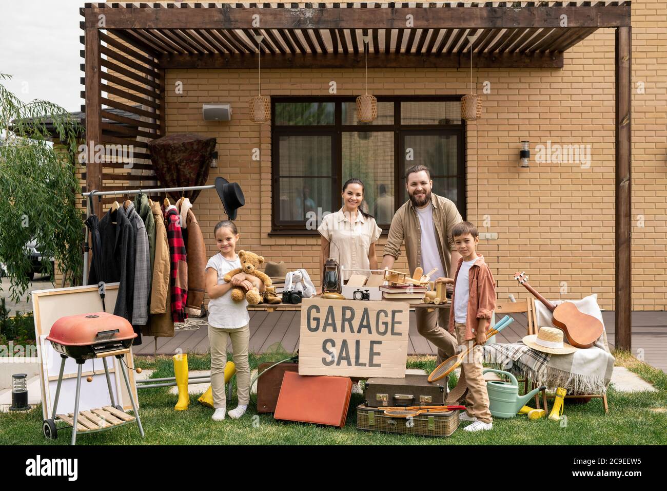 Ritratto di famiglia sorridente amichevole con i capretti carini che vendono insieme roba alla vendita del garage nel cortile Foto Stock