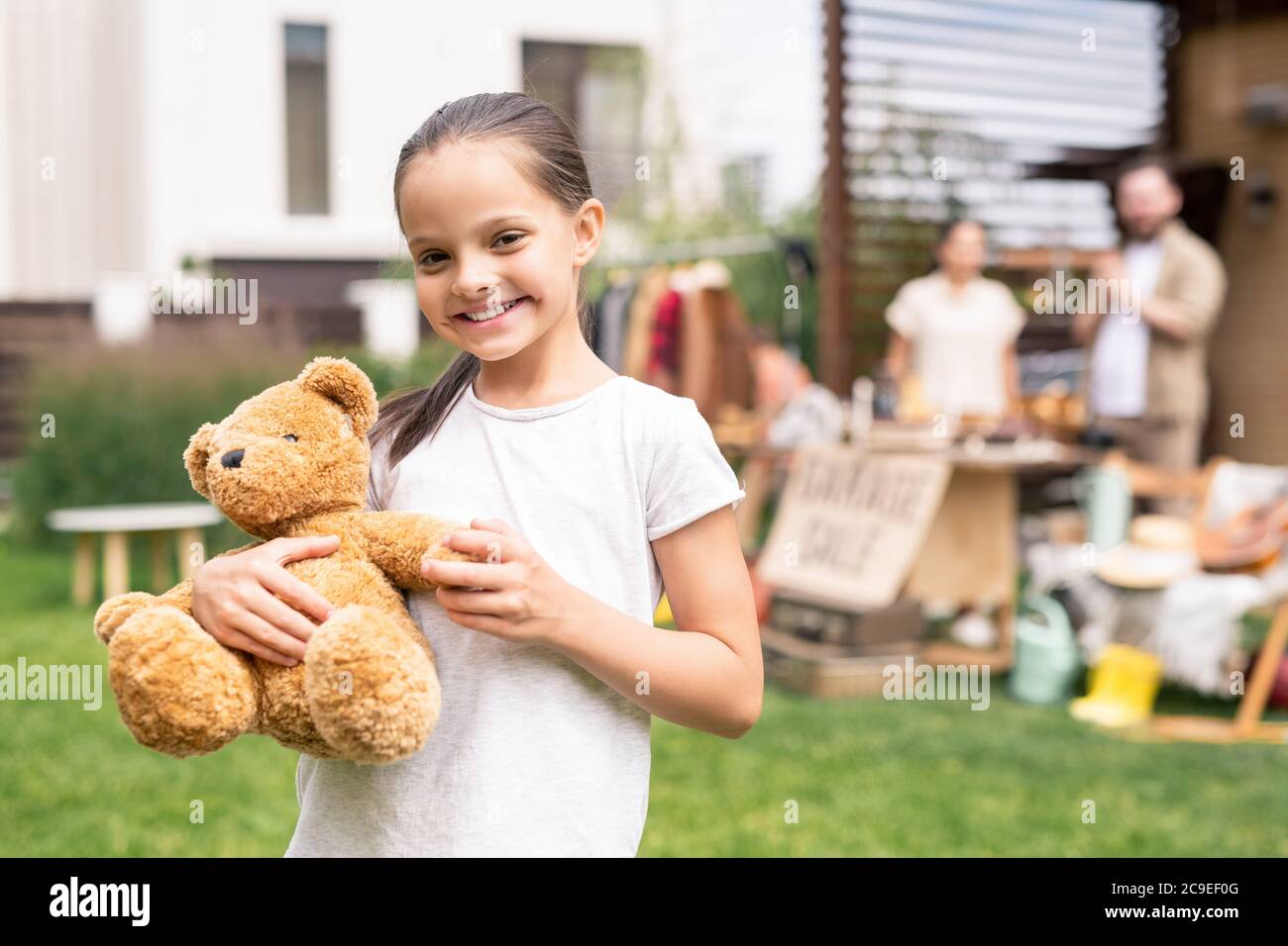 Ritratto di sorridente bella ragazza abbracciando l'orso giocattolo acquistato in garage vendita Foto Stock
