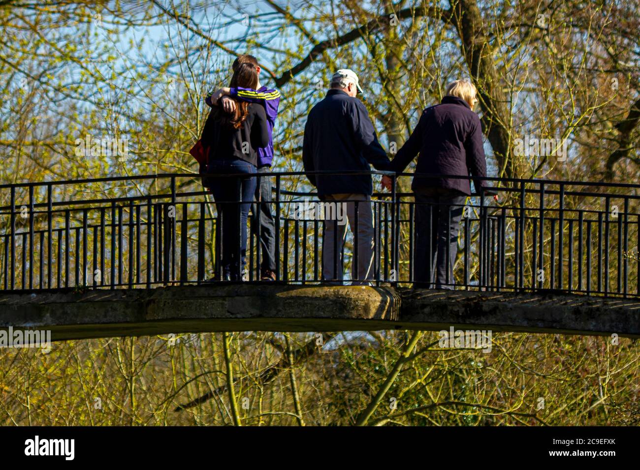 Oxford, UK 03/19/2011: Differenza di norme tra baby boomer e millennials. Una giovane coppia sta baciando su un ponte in un parco mentre un colpo di stato anziano Foto Stock