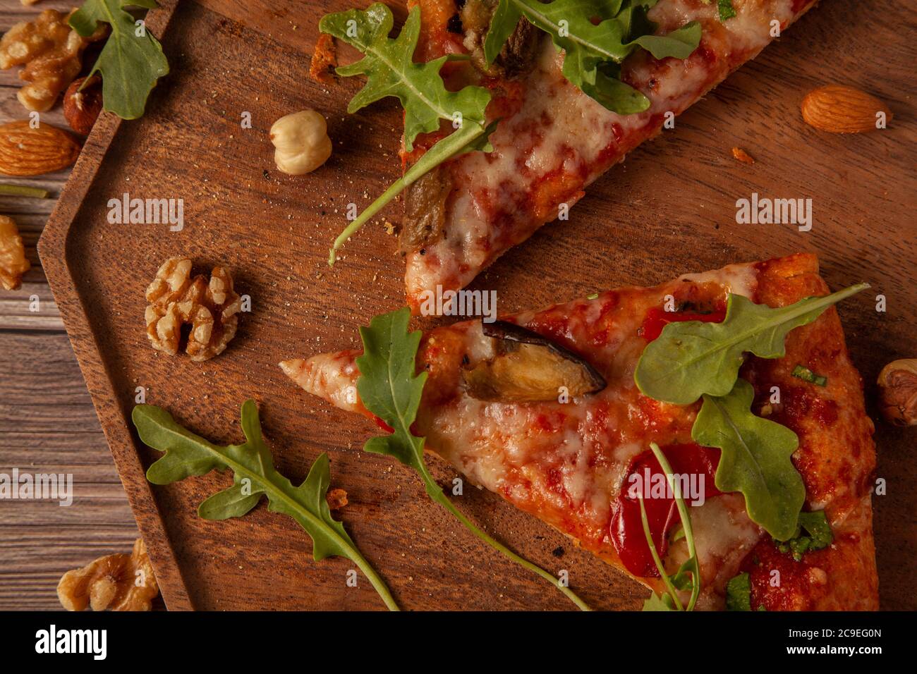 Piatto immagine ravvicinata di formaggio vegetariano e pizza di pomodoro decorata con foglie di rucola fresche e fette di piante d'uovo alla griglia. E' servita su legno Foto Stock