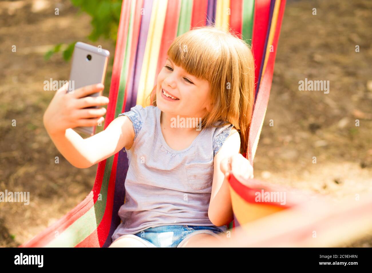 Carino bambina che cammina all'aperto e riposa su amaca in estate foresta prendendo selfie o fare videochiamata con il telefono cellulare. Foto Stock