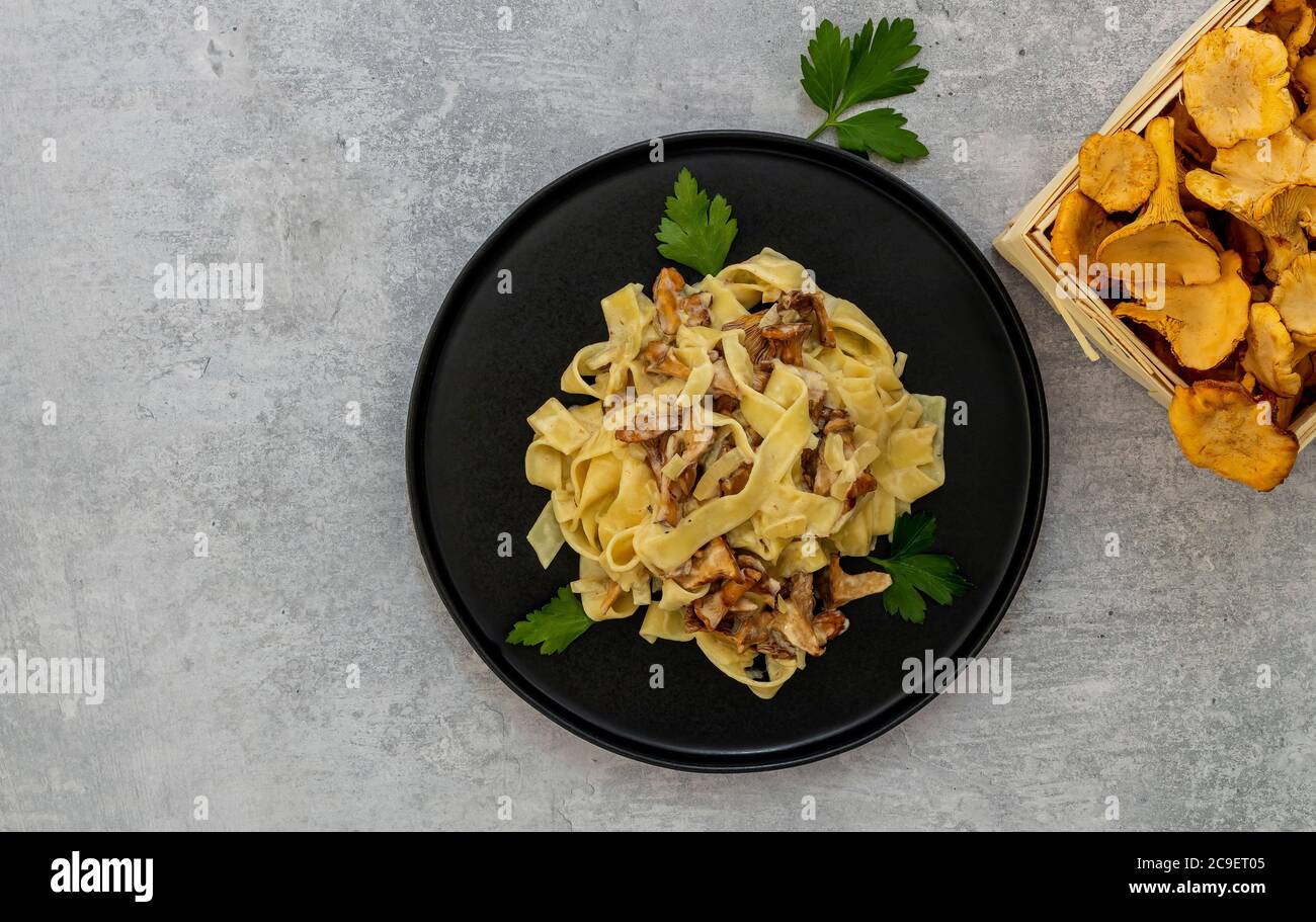 Tagliatelle di pasta italiana con funghi chanterelle e prezzemolo in un piatto nero Foto Stock