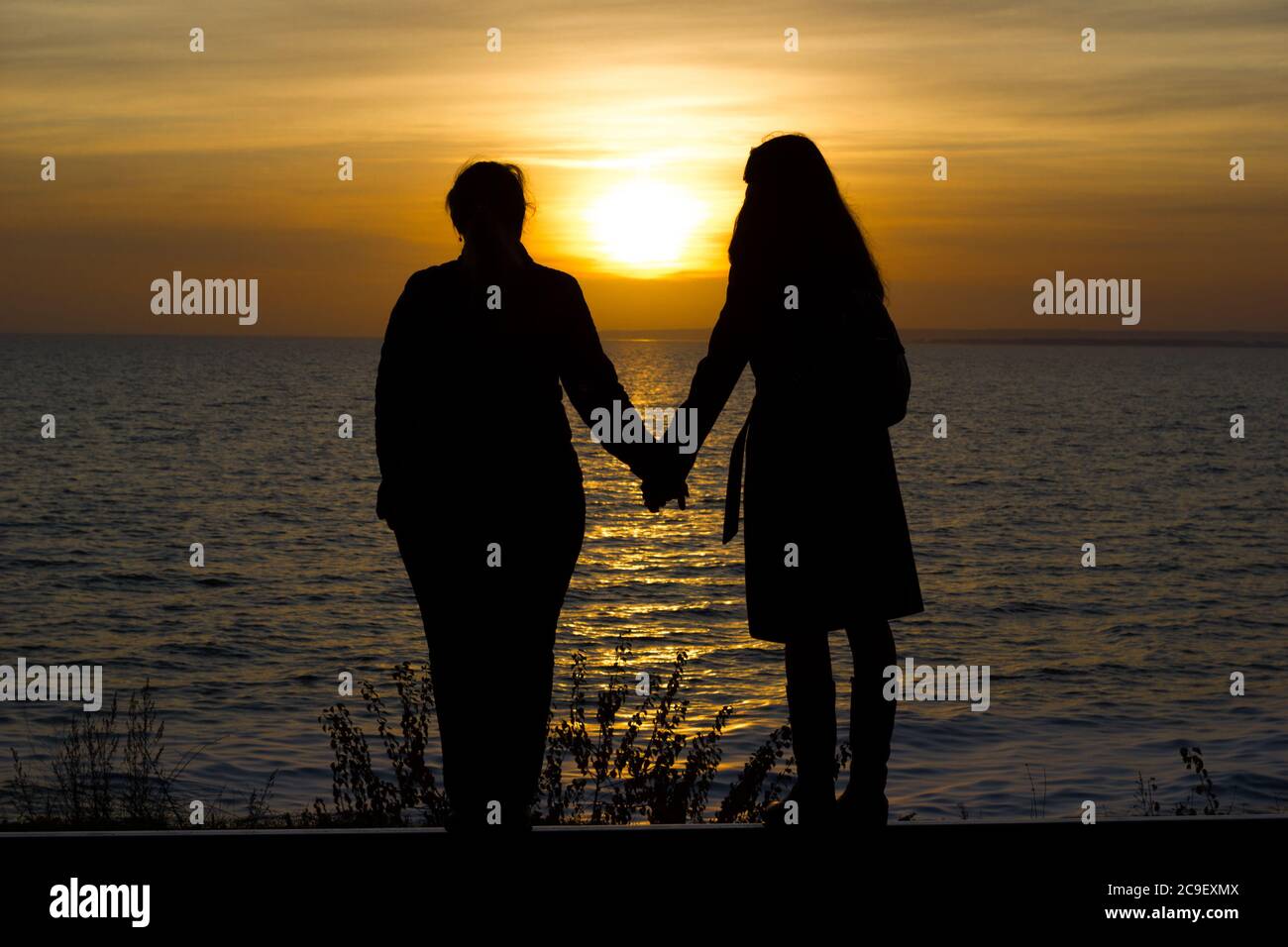 Girlfriends sono in piedi sulle rotaie ferroviarie tenendo le mani su uno sfondo tramonto - viaggio, depressione, stile di vita Foto Stock