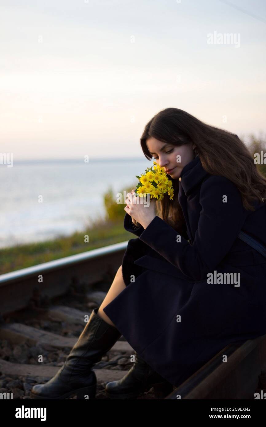 La ragazza cammina sulle rotaie ferroviarie in un cappotto con fiori - viaggio, depressione, stile di vita, amore Foto Stock