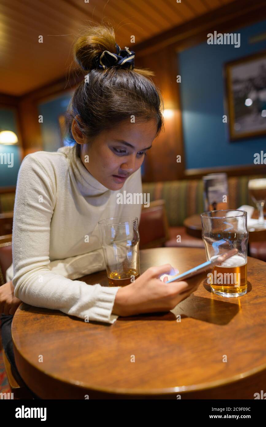 Giovane bella donna turistica asiatica utilizzando il telefono cellulare al ristorante con due bicchieri di birra Foto Stock