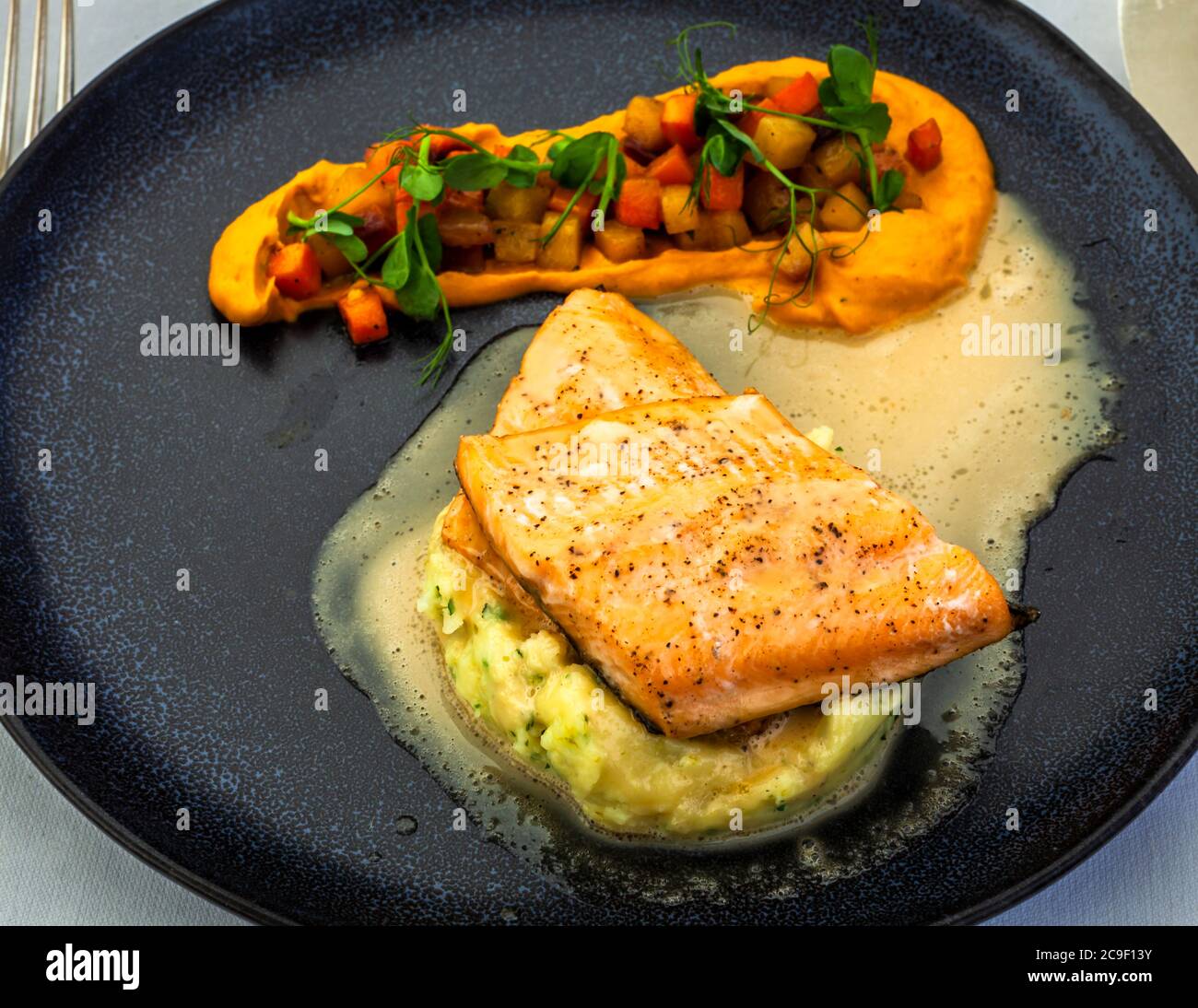 Un filetto di salmone croccante alla griglia si trova su un purè di patate alle erbe in una leggera salsa al burro, accanto a un purè di patate dolci e carote ricoperto di peperoni e patate a dadini, all'Hotel Florhof a Zurigo, Svizzera. Il piatto è stato creato dallo chef de cuisine Marc Homberger. Foto Stock