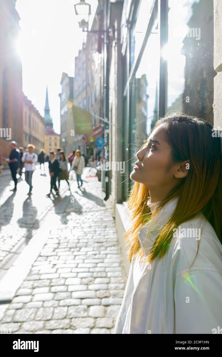 Profilo vista di giovane bella donna turistica asiatica appoggiata contro il muro di vintage edificio nelle strade Foto Stock