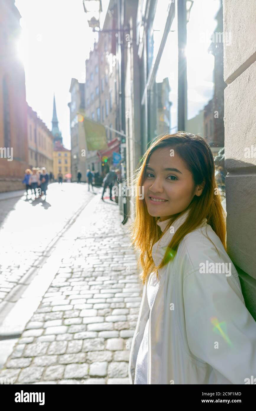 Felice giovane bella donna turistica asiatica appoggiata contro il muro nelle strade della Svezia Foto Stock