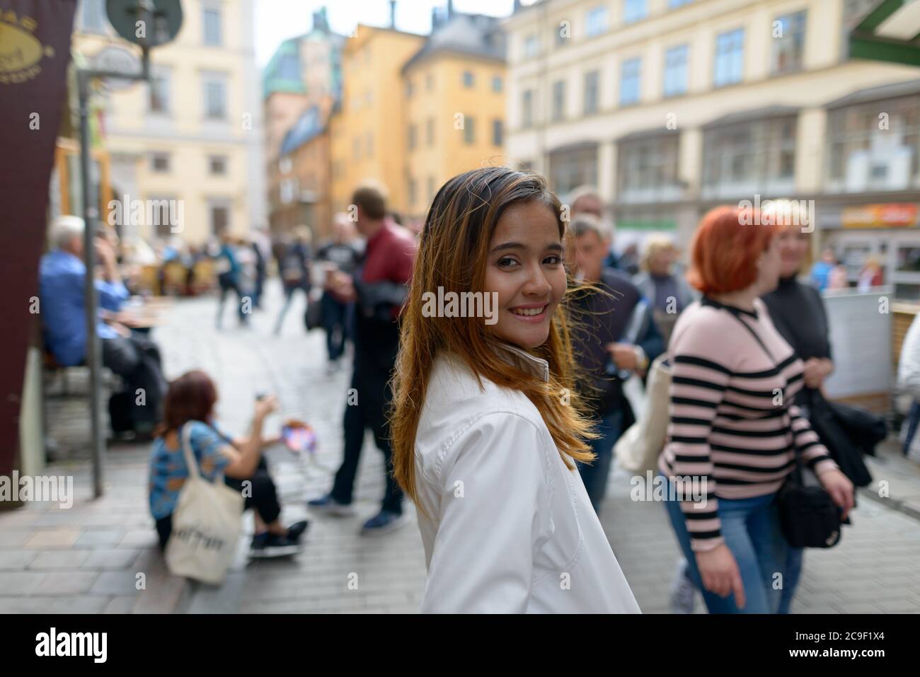 Felice giovane bella donna turistica asiatica sorridente contro la vista della piazza della città vecchia in Svezia Foto Stock