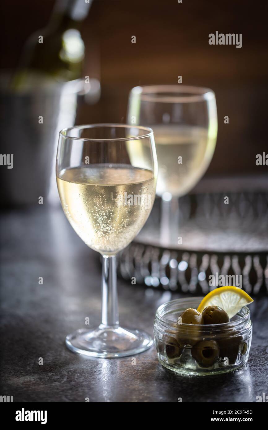 Vino bianco servito su vassoio di metallo brunito con piatto di olive. Sfondo scuro. Verticale Foto Stock