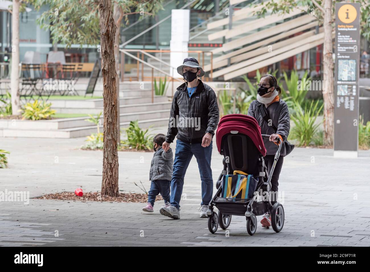 Sydney, Australia, luglio 2019: Una giovane famiglia asiatica di tre persone cammina attraverso Darling Square a Sydney, tutti indossando maschere per il viso durante la pandemia del Covid-19 Foto Stock