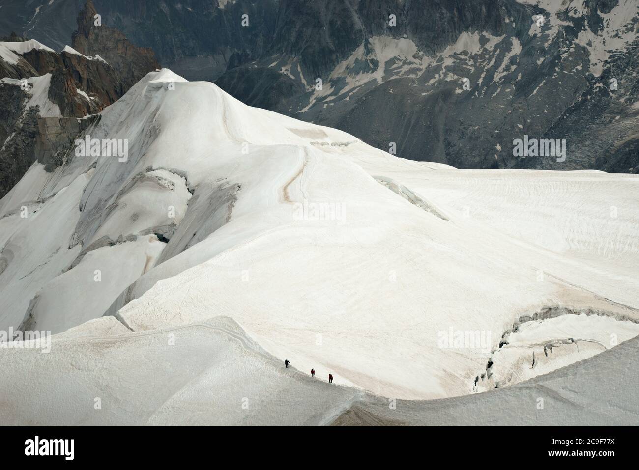 Tre scalatori che camminano lungo una dorsale innevata, in cima alle montagne. Sono incuriositi dalla scala del paesaggio epico intorno a loro. Foto Stock