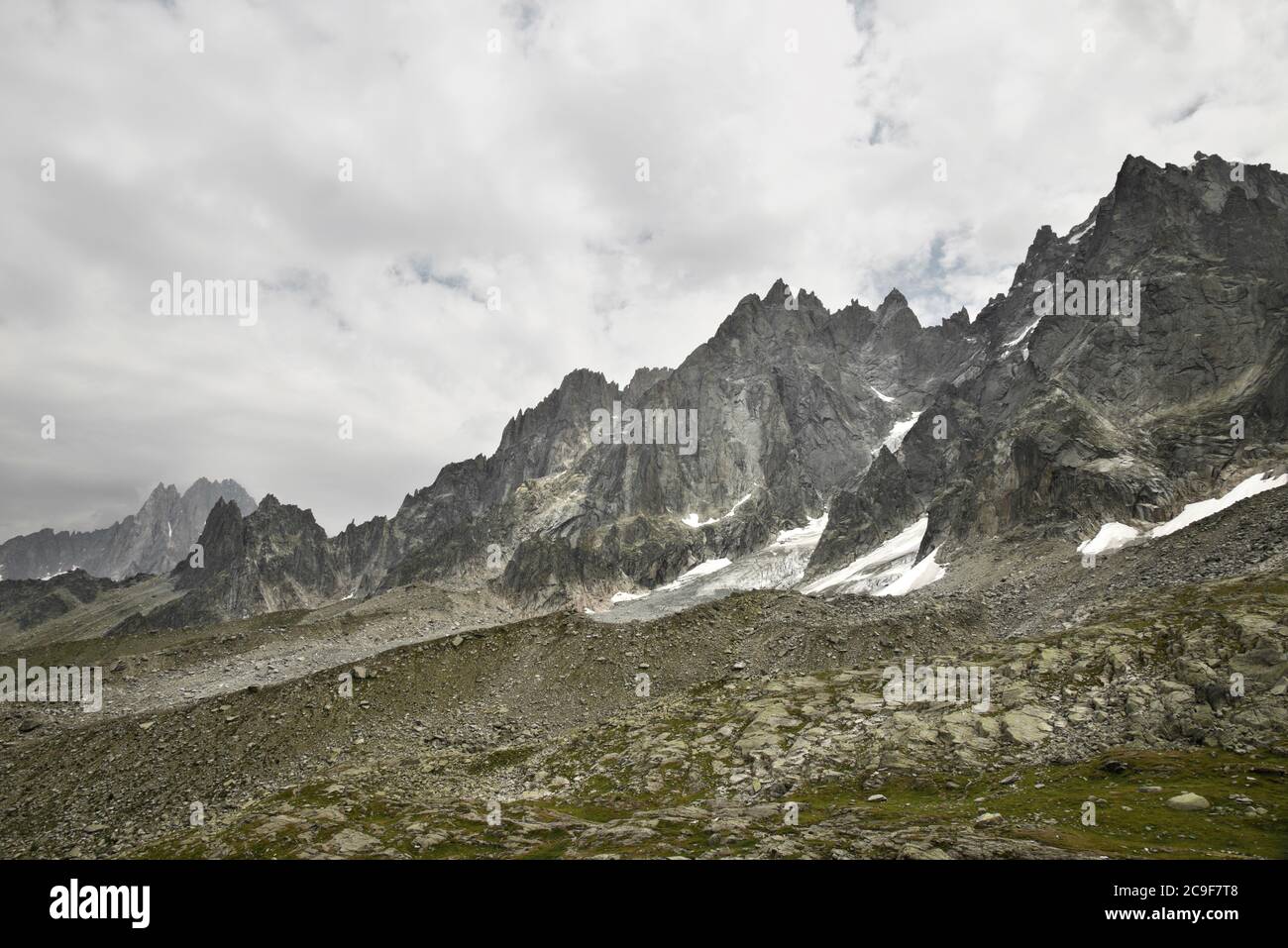 Guardando attraverso le cime rocciose e affilate di una catena montuosa. Cielo grigio, nuvoloso e macchie di neve tra le rocce. Foto Stock