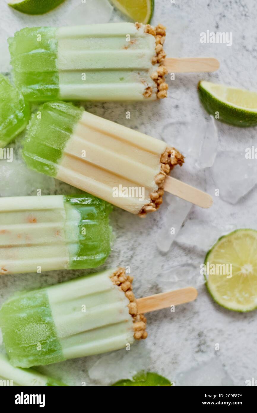 Lime e panna fatta in casa popsicles o gelati messi con cubetti di ghiaccio su sfondo di pietra grigia Foto Stock