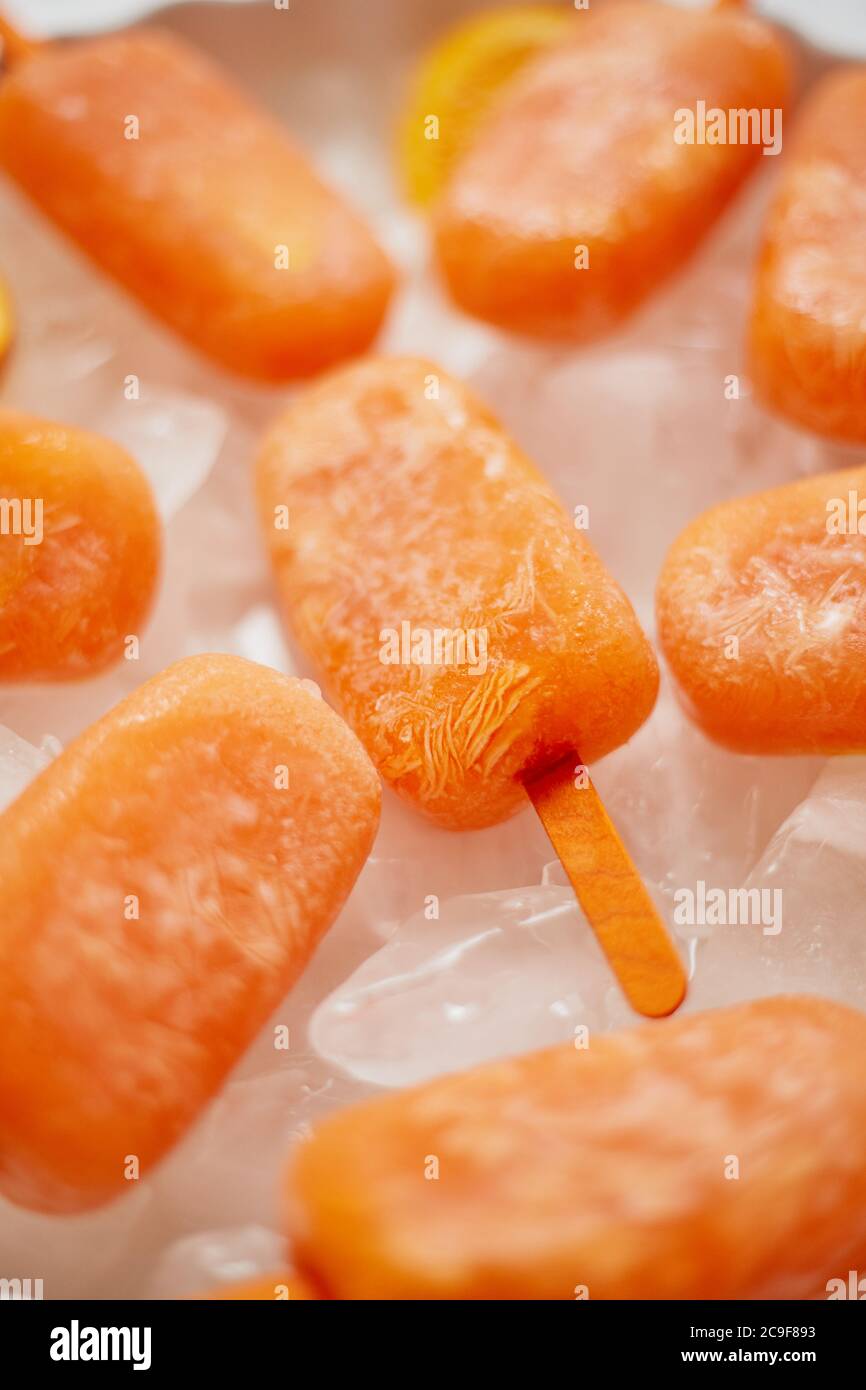 Pop sicle surgelate fatte in casa con arance fresche oragniche poste con cubetti di ghiaccio sul tavolo di marmo Foto Stock
