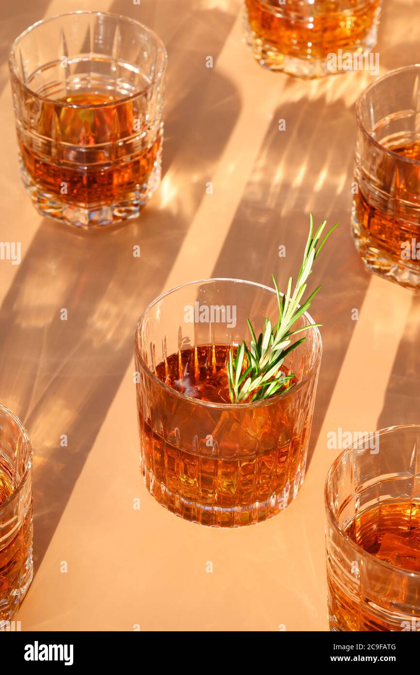 Molti bicchieri di whisky freddo serviti in rocce con rosmarino su sfondo beige trendy. Formato verticale. Foto Stock
