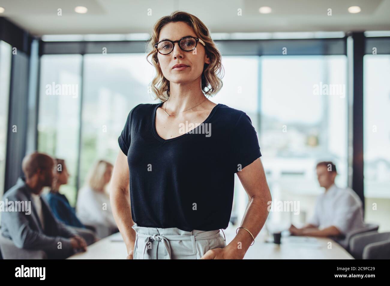 Ritratto di una donna d'affari sicura in carica con colleghi che parlano sullo sfondo nella sala riunioni. Foto Stock