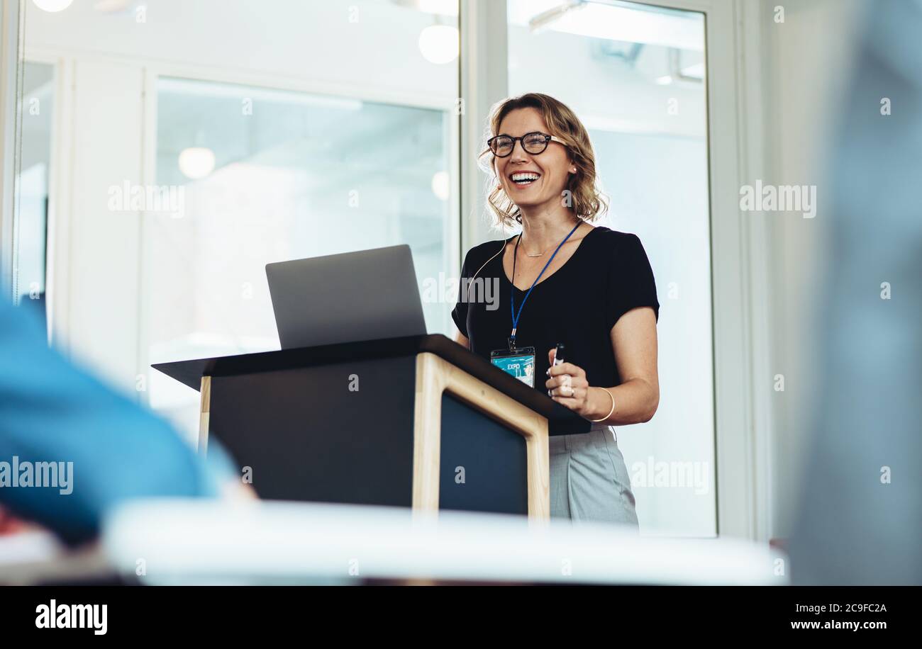 Donna d'affari in piedi sul podio con un portatile che dà un discorso. Donna di successo professionale di affari che affronta un seminario. Foto Stock