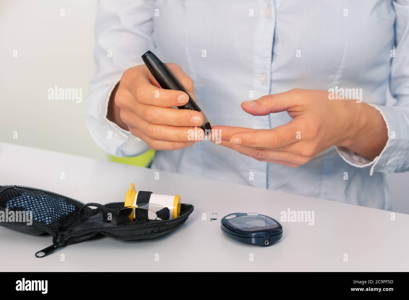 Chiudi la foto delle mani della donna che fanno un test dello zucchero per il diabete seduto al tavolo Foto Stock